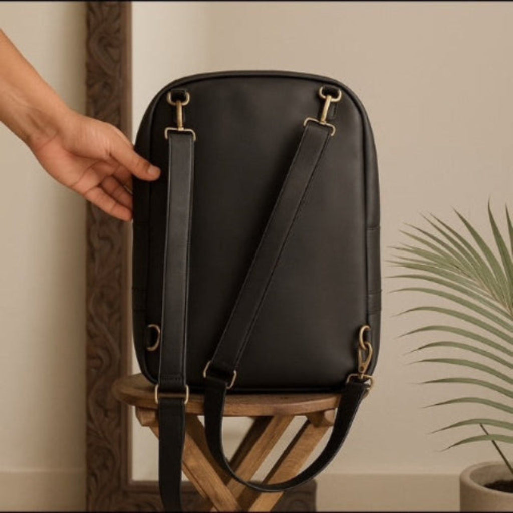 Black backpack with gold hardware on a wooden stool against a neutral wall.