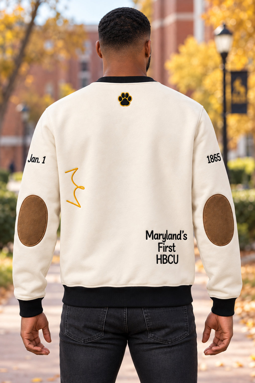 Model wearing a cream Bowie State sweatshirt with brown elbow patches, a paw print below the collar, and ‘Maryland’s First HBCU’ lettering.