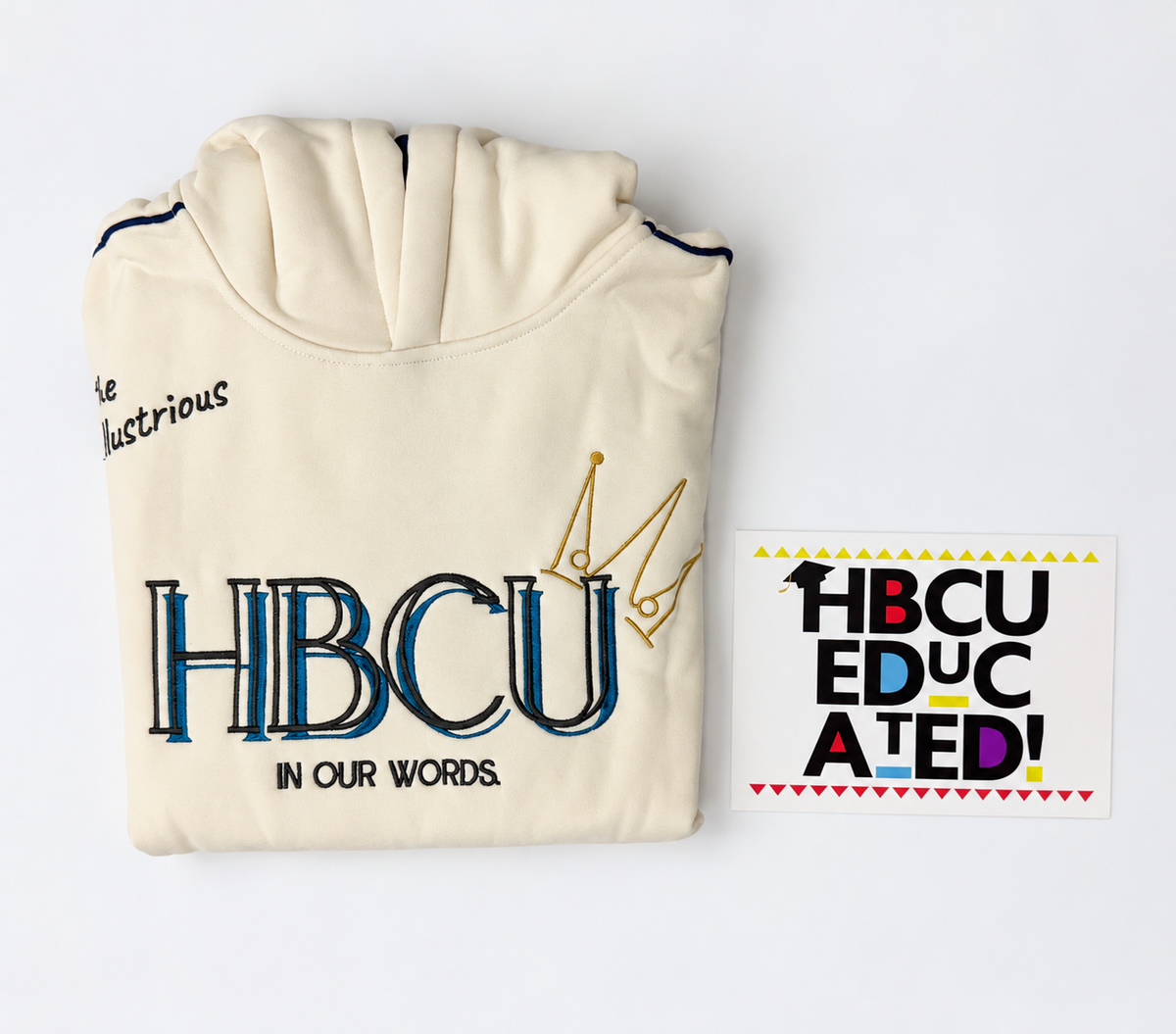 A folded cream-colored sweatshirt with 'HBCU' printed in large navy and gold lettering, shown alongside a matching sticker on a clean white background.