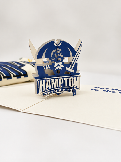 A 3D pop-up cardboard sign for the Hampton Pirates, featuring a blue and white pirate emblem with crossed swords and the text 'HAMPTON PIRATES', displayed on an open cream-colored envelope.