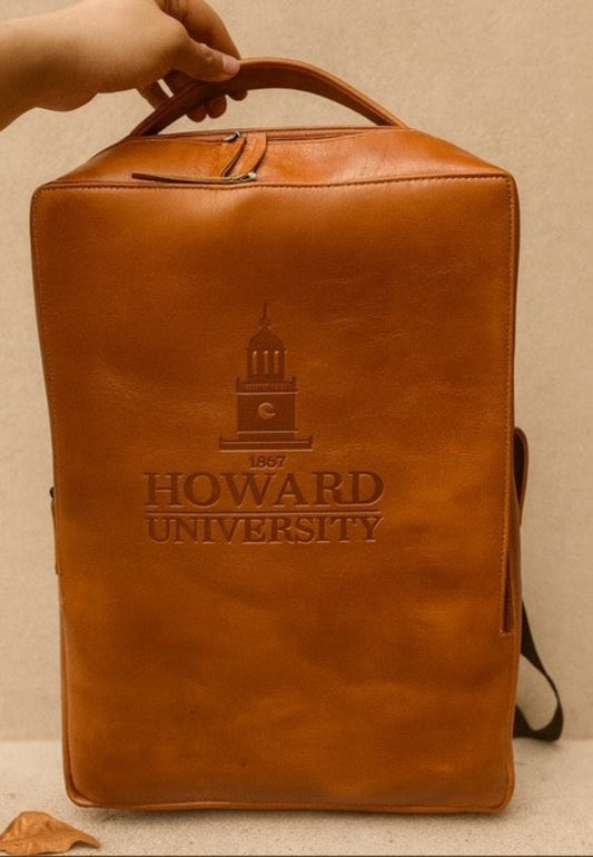 Brown leather backpack with 'Howard University' embossed on it, held by a hand against a beige background.