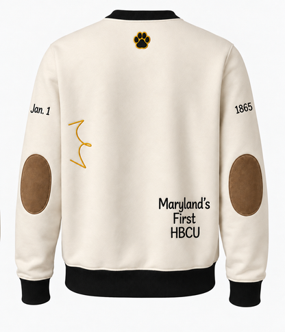 Back of the cream Bowie State sweatshirt with a gold paw print at the neckline, “Jan. 1” and “1865” on the sleeves, tan suede elbow patches, and “Maryland’s First HBCU” in black lettering at the lower right.