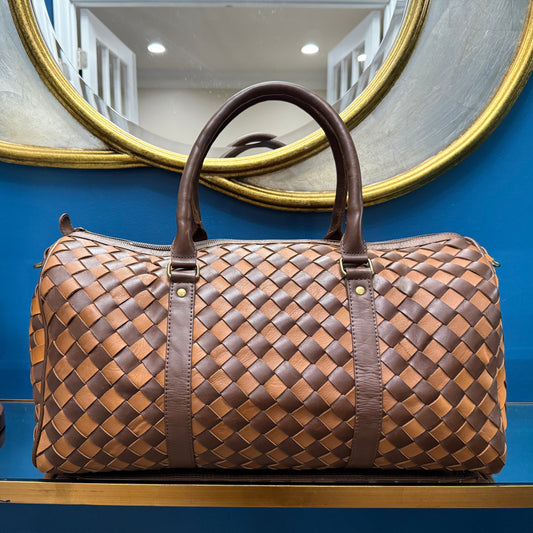 Brown woven handbag on a blue surface with a mirror and lamp in the background
